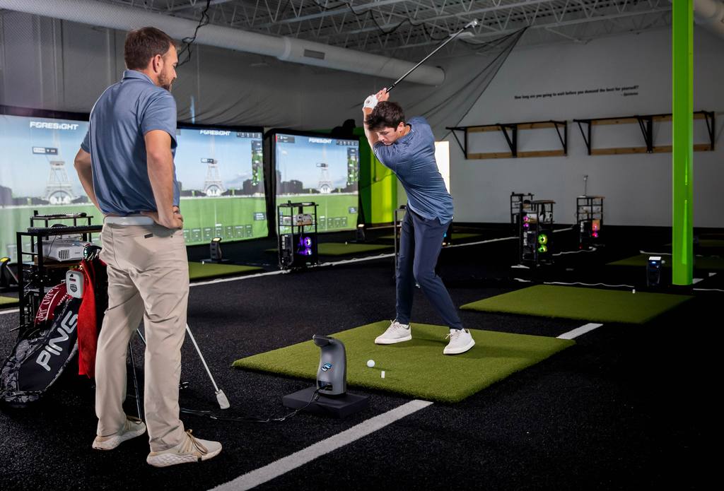 Luke Benoit watching a student's swing on the RYP Academy simulator floor