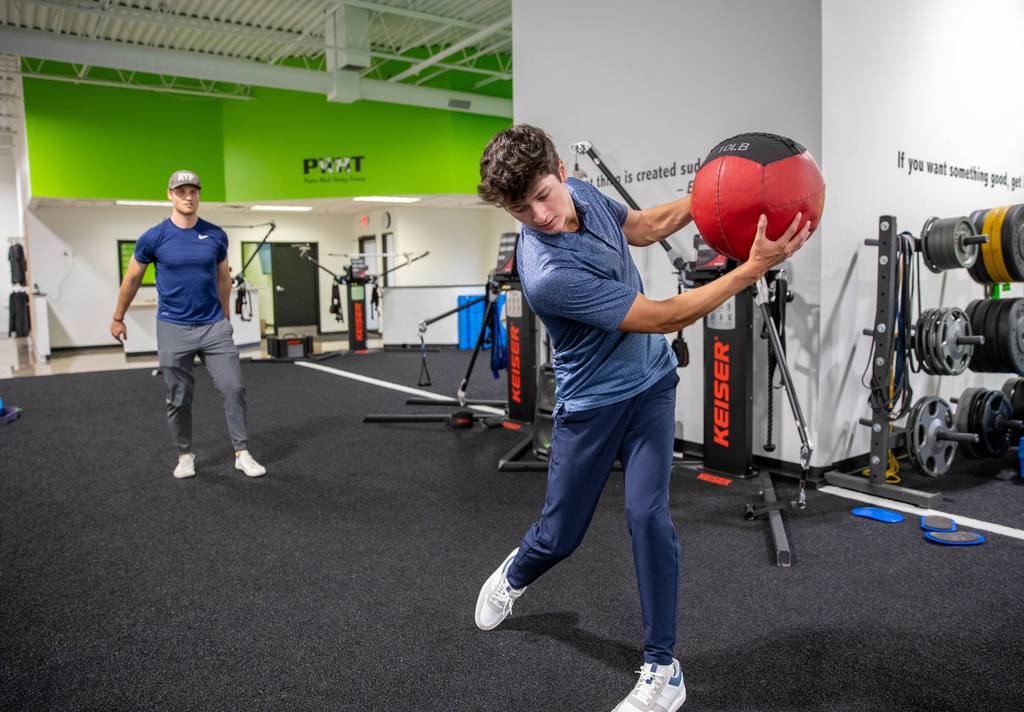 A junior athlete driving a medicine ball through a rotational throw in the gym